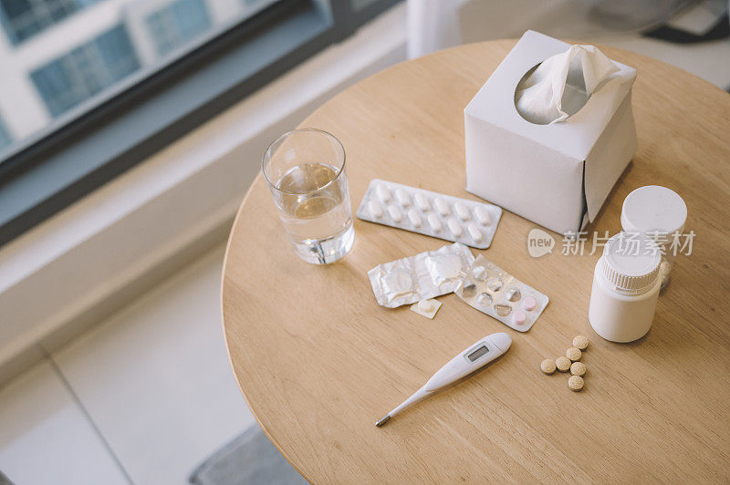 medical pills ,bottles , tissue box, thermometer and a glass of water on the table